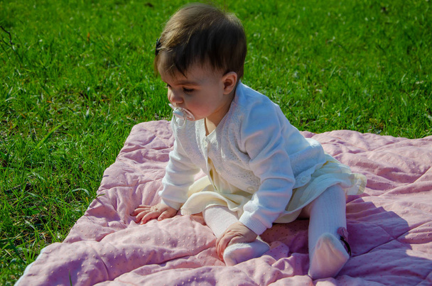 Baby in bright clothes on a pink plaid on green grass in the park. Newborn baby outside on a warm day. Little girl plays on a plaid on a green lawn in spring - Fotoğraf, Görsel