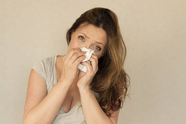 woman sneezes and looks at camera against grey background. concept of allergy or flu - Foto, afbeelding