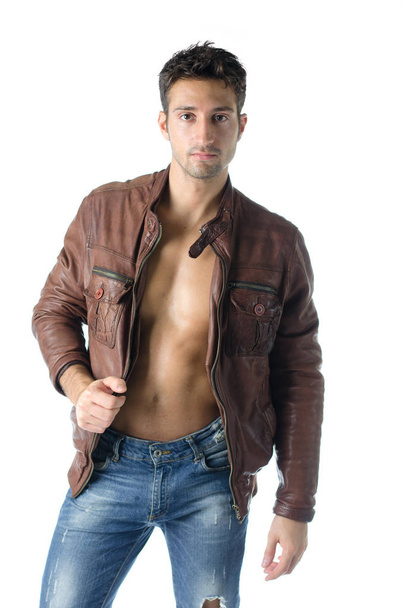 Attractive young man wearing leather jacket on naked torso and blue jeans, isolated on white - Zdjęcie, obraz