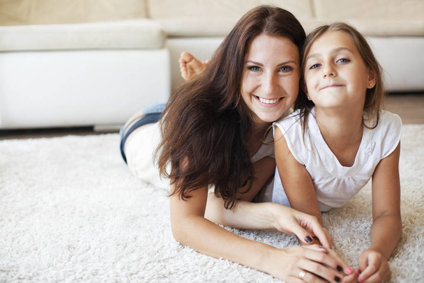 Mother with her preteen daughter having fun on a white carpet in living room at home - Foto, imagen