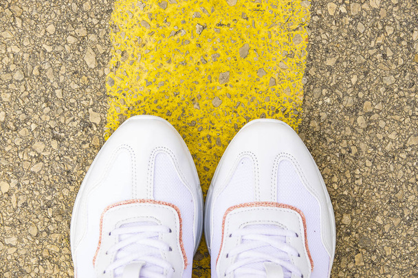 Womens feet on the road. White sneakers on asphalt top view - Foto, Imagem
