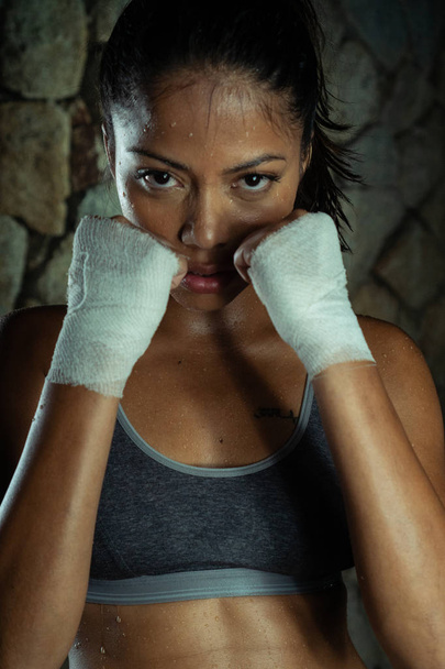 Σέξι μελαχρινή γυμναστήριο υγρή γυναίκα στο γυμναστήριο. Πορτρέτο της ελκυστική γυναίκα σε αθλητικά είδη που θέτουν σε στάση μάχης με ψηλά χέρια - Φωτογραφία, εικόνα