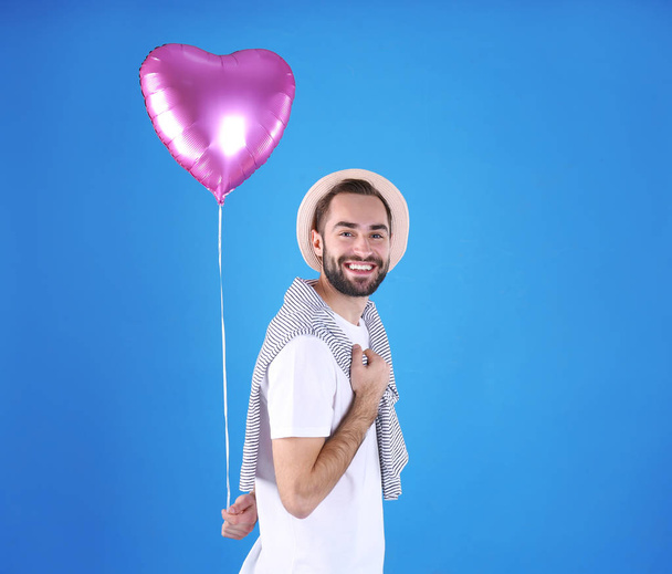 Portrait of young man with heart shaped balloon on color background - Foto, immagini