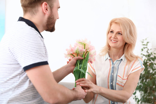 Young man congratulating his mature mom at home. Happy Mother's Day - Фото, изображение