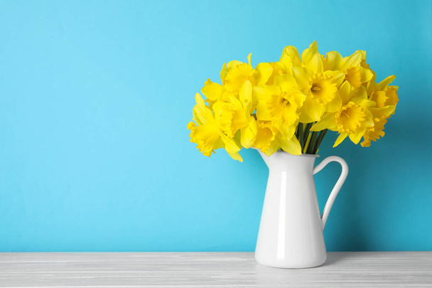 Bouquet of daffodils in jug on table against color background, space for text. Fresh spring flowers - Foto, Imagem