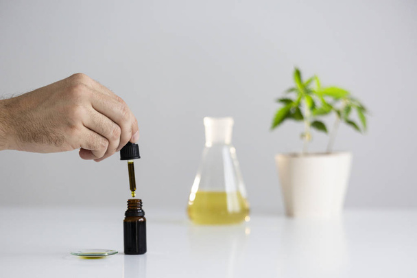 Hand dropping CBD oil from pipette to the bottle - Photo, Image