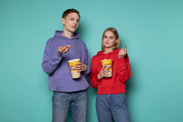 Jeune couple indigné en vêtements décontractés regarder un film contradictoire, tenant seau de maïs soufflé
 - Photo, image
