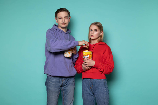 Молода приваблива людина в блакитному светрі краде попкорн від своєї дівчини, красива блондинка дивиться на нього з обуренням
 - Фото, зображення