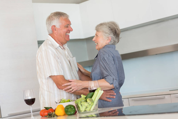 Happy senior couple hugging while preparing a meal at home in the kitchen - Foto, Imagem