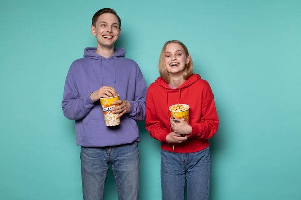 glückliche Freunde, schönes blondes Mädchen und Mann in lila Kapuzenpulli, die einen Komödienfilm mit Popcorn in den Händen ansehen - Foto, Bild