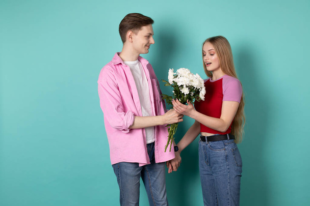 Bonito jovem na camisa rosa dá um buquê de flores brancas para sua bela namorada loira
 - Foto, Imagem
