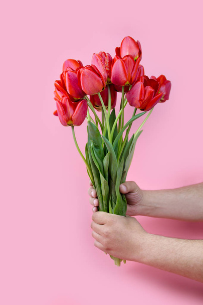Mans hand reaching out a bunch of yellow tulips on blue background with copy space - Foto, afbeelding