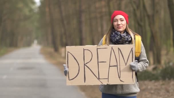 Κορίτσι ωτοστόπ μείνει σε άδειο δρόμο σε ξύλο με αφίσα όνειρο - Πλάνα, βίντεο