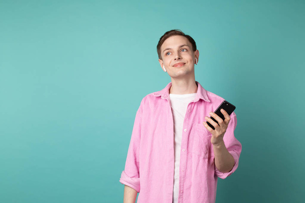 Young handsome man in pink shirt with phone in hands and white earphones - Foto, Imagen