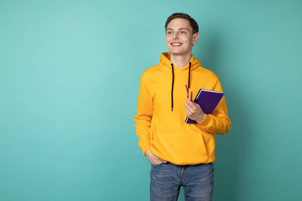 Young cheerful man wearing yellow hoodie, holding purple notebook and pen. Inspiration to create - Foto, Imagem
