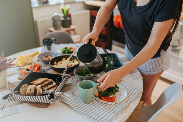 Close-up van ontbijttafel en vrouw hand met een grote koffiefilter glazen mok, poring koffie. - Foto, afbeelding