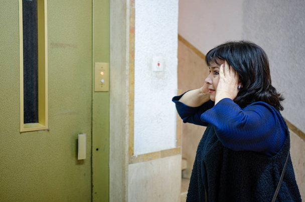 L'attaque de panique provoque un fort mal de tête pour la femme claustrophobe. Elle reste devant l'ascenseur dans une maison d'habitation
. - Photo, image
