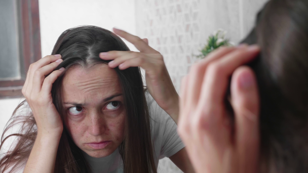 junge Frau blickt im Badezimmer vor dem Spiegel auf ihre Haare. - Filmmaterial, Video