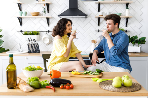 Young cute couple - a boy and a girl romantically spend time in the kitchen. A couple drinks alcohol and prepares a salad. Young cute smiling couple cooking together at kitchen at home - Foto, afbeelding