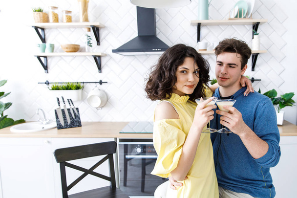 Young cute couple - a boy and a girl romantically spend time in the kitchen. A couple drinks alcohol and prepares a salad. Young cute smiling couple cooking together at kitchen at home - Fotoğraf, Görsel