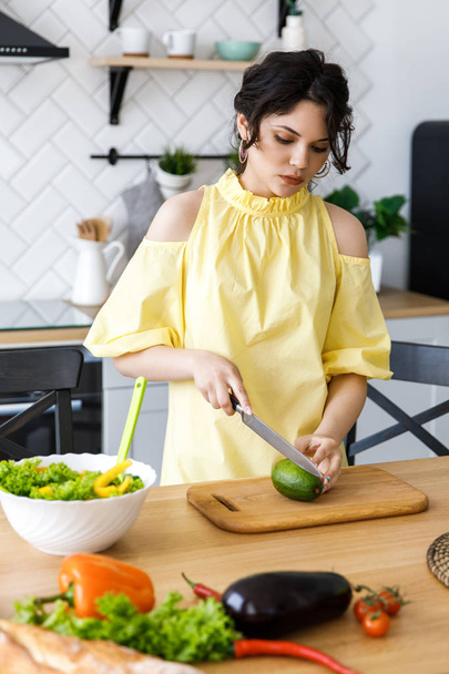Young pretty woman cuts an avocado on a wooden salad board. Cooking. Preparation of fresh vegetable salad - Fotoğraf, Görsel
