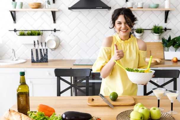 Jonge mooie vrouw snijdt een avocado op een houten saladebord. Koken. Bereiding van verse groenten salade - Foto, afbeelding