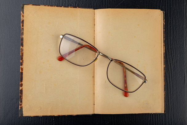 Old book and glasses on a dark wooden table. Forgotten publishin - Foto, imagen