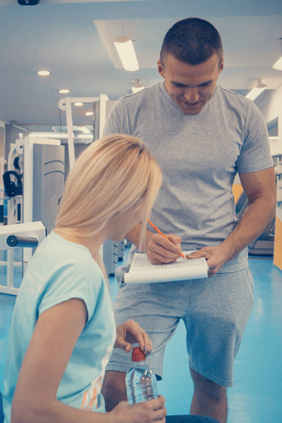 Mujer y hombre en el gimnasio, deportista escribiendo notas para el entrenamiento
. - Foto, Imagen