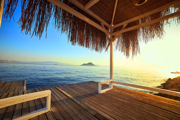 Bungalov na moři při západu slunce. Dřevěné pavilony na břehu písečné pláže-Bodrum, Turecko  - Fotografie, Obrázek