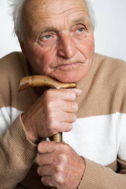 Το πορτρέτο ενός παλιού θλιβερού ανθρώπου που έβαλε το κεφάλι του στο χερούλι ενός ξύλινου μπαστουνιού. - Φωτογραφία, εικόνα