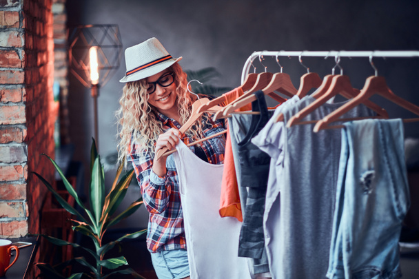 Pretty young woman in hat and glasses  is choosing new outfit for summer - Photo, Image