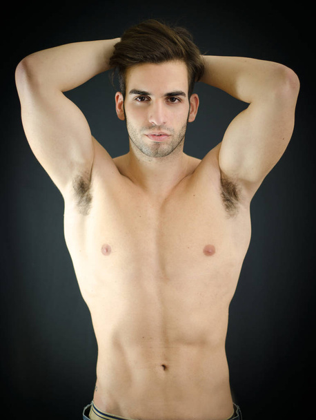Sexy shirtless young man with arms up behind his head, showing muscular torso, pecs and abs - Photo, image
