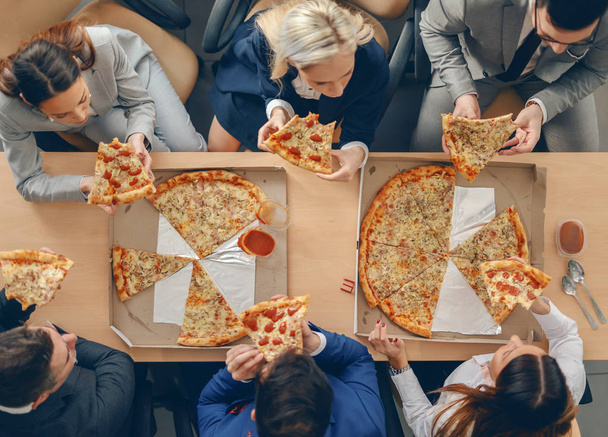 von oben: Geschäftsleute in formeller Kleidung sitzen am Tisch und essen Pizza zum Mittagessen. - Foto, Bild