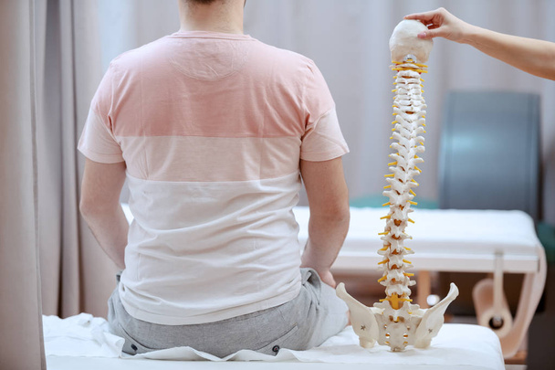Jovem médico atraente segurando modelo da coluna vertebral e truing para perceber onde é o lugar doloroso do paciente
. - Foto, Imagem
