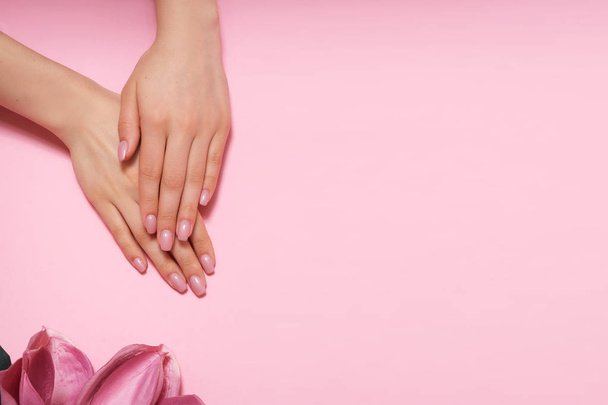 Manicura. Hermosas y delicadas manos sobre fondo rosa con flores rosadas
. - Foto, imagen