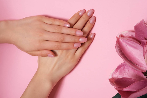 Manicure. Mooie en delicate handen op roze achtergrond met roze bloemen. - Foto, afbeelding