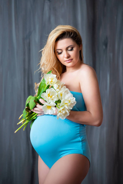 Beautiful young pregnant blonde woman holding flowers white tulips in her hands. Spring mood, freshness, women's Day, health and beautiful pregnancy - Photo, image