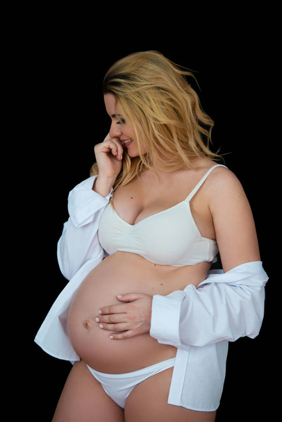 Beautiful smiling blonde pregnant woman in white clothes on a black background. Women's health and happy pregnancy - Foto, afbeelding