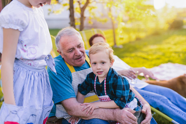 Photo de grand-mère et grand-père s'amusant avec leur petit-fils. Assis dans leur jardin et souriant
. - Photo, image