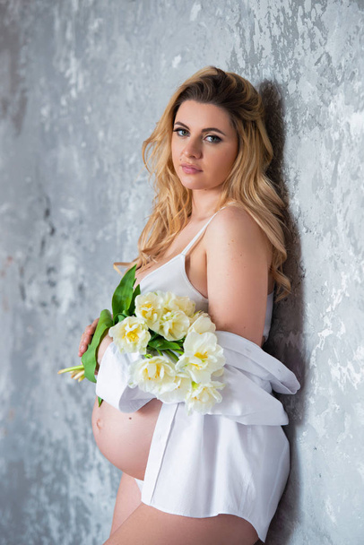 Beautiful young pregnant blonde woman love flowers white tulips. Spring mood, freshness, women's Day, health and beautiful pregnancy - Foto, Imagen