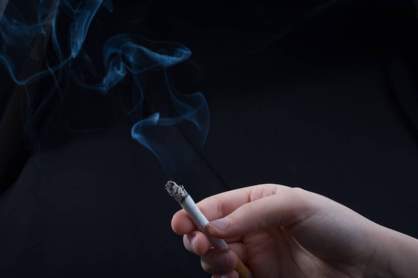 Hand hält rauchende Zigarette auf schwarzem Hintergrund - Foto, Bild