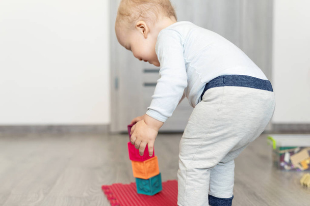 Χαριτωμένο αξιολάτρευτο Καυκάσιος μωρό αγόρι παίζει πολύχρωμα παιχνίδια στο σπίτι. Ευτυχισμένο παιδί με διασκεδαστικό πύργο κτίριο από μαλακό καουτσούκ κύβους. Η ανάπτυξη των παιδιών και η αίσθηση της χαλαρίας - Φωτογραφία, εικόνα