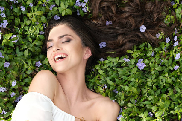 Close up of woman lying down on the grass. Beautiful make up and shiny hair in nature. - Photo, Image