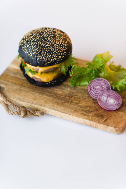 schwarzer Cheeseburger auf Hackbrett, grauer Hintergrund. - Foto, Bild