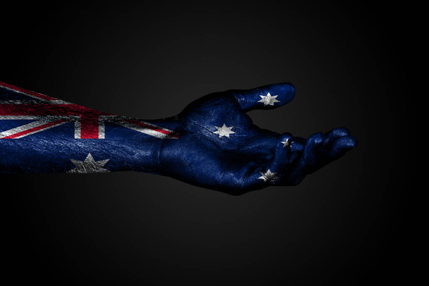 Ένα απλωμένο χέρι με μια βαμμένη σημαία της Αυστραλίας, ένα σήμα βοήθειας ή ένα αίτημα, σε σκοτεινό φόντο - Φωτογραφία, εικόνα