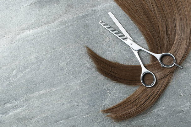Flat lay composition with brown hair, thinning scissors and space for text on grey background. Hairdresser service - Photo, image