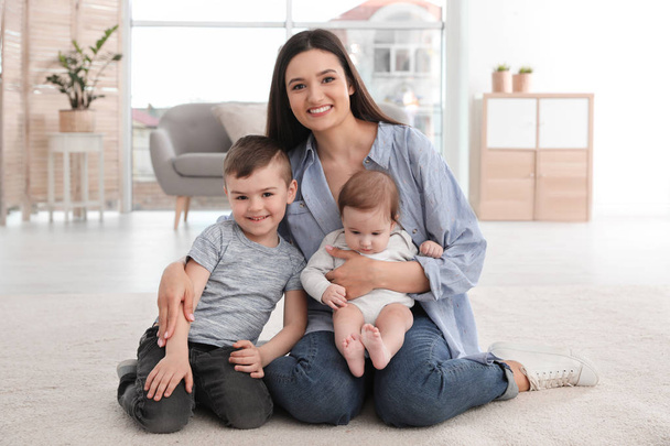 Young mother with her children sitting together on floor at home - Photo, Image