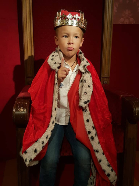 Un petit garçon dans une couronne et un manteau est prêt à régner avec l'index levé
 - Photo, image