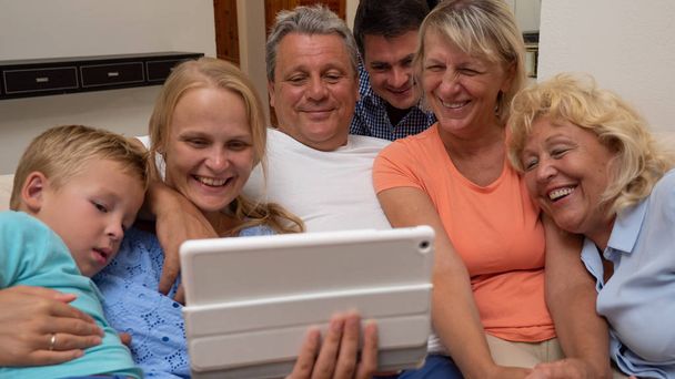 Duża rodzina ogląda coś śmiesznego na podkładce, blisko obok siebie - Zdjęcie, obraz