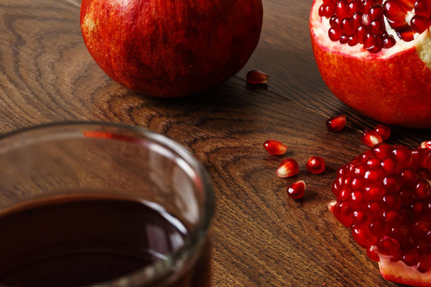red pomegranate fruits, seeds and glass with juice on a dark sur - Photo, Image